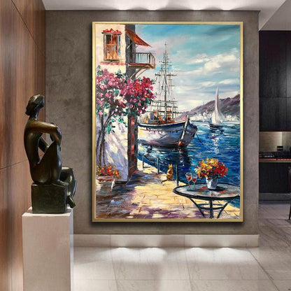 May include: A painting of a sailboat docked in a harbor with a building and flowers in the foreground. The sky is blue with white clouds and the water is a deep blue.
