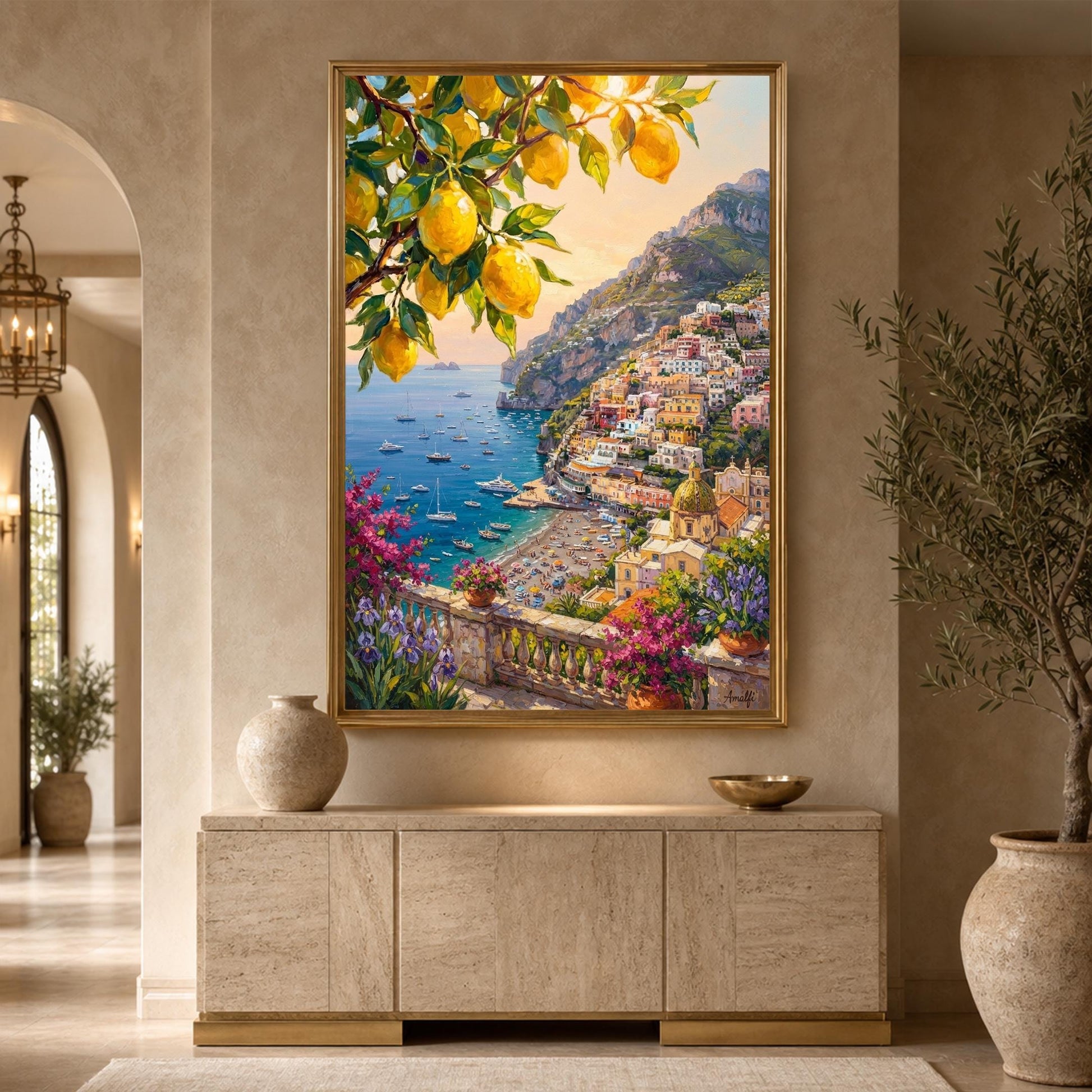 A large framed canvas painting of a Mediterranean coastal town with lemons hangs on a beige wall above a stone console table in a styled interior room.